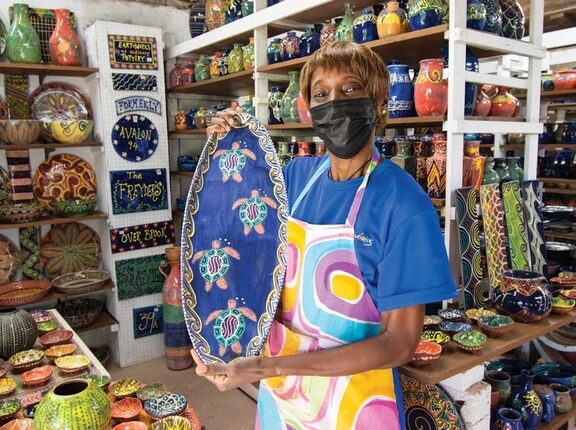Staff member holding ceramic piece with colorful pottery in background